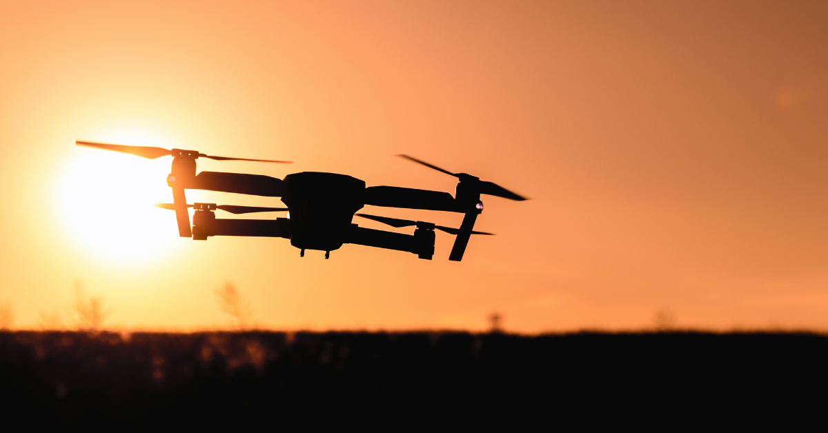 a surveying drone hovering over the ground as the sun sets in the background